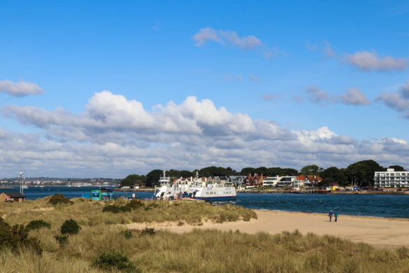 People walking on Shell Bay with Sandbanks Ferry behind