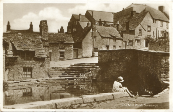 An old postcard of a woman sitting by the mill pond in Swanage