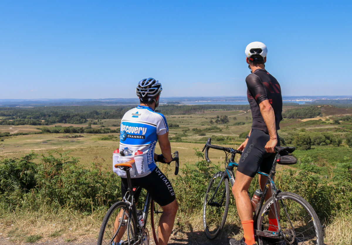 Two cyclists sitting on bikes looking at view over Studland from The Viewpoint near Corfe