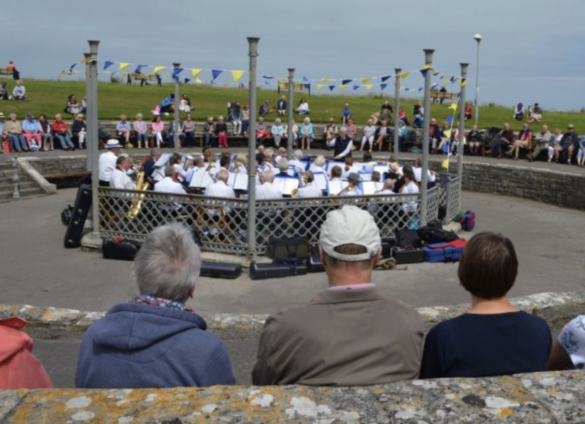 People watching The Swanage Town band play in a roofless bandstand