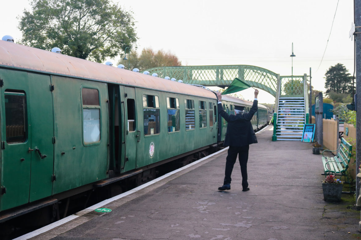 Volunteer conductor waving a diesel train off with a flag from Corfe Castle station