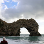 Boy in a white bobble hat looking at Durdle Door from beach