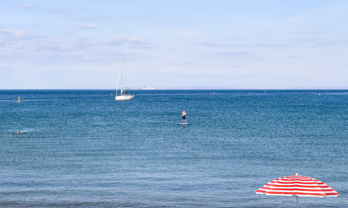 Stripy red and white parasol and paddle boarder at Swanage Beach