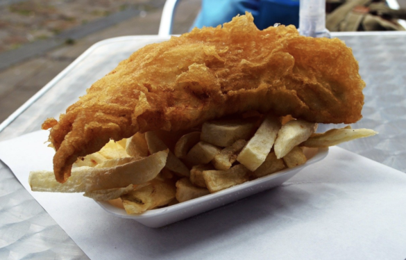 Battered cod on top of chips in takeaway tray