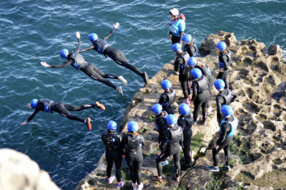 People in wetsuits and helmets jumping into the sea