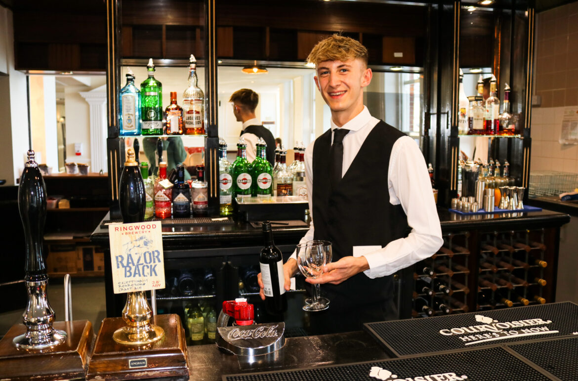 Man carrying wine glasses behind the bar at The Grand in Swanage
