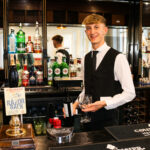 Man carrying wine glasses behind the bar at The Grand in Swanage