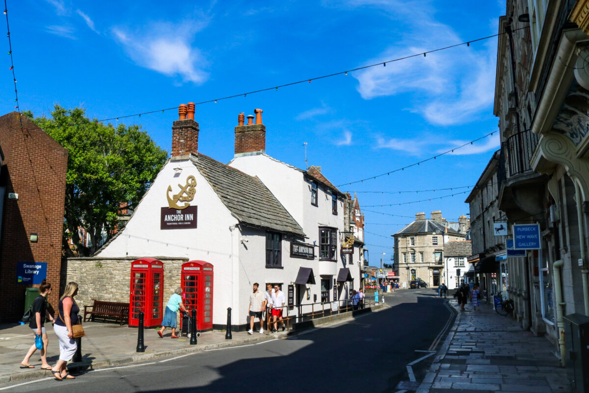People walking past the Anchor Inn and Swanage library on a sunny day
