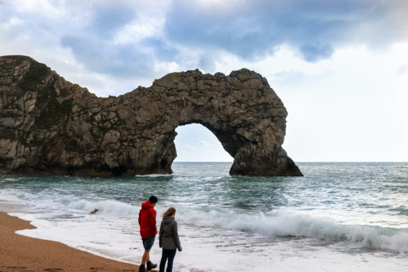 Two people standing on the shingle beach of Durdle Door in Dorset