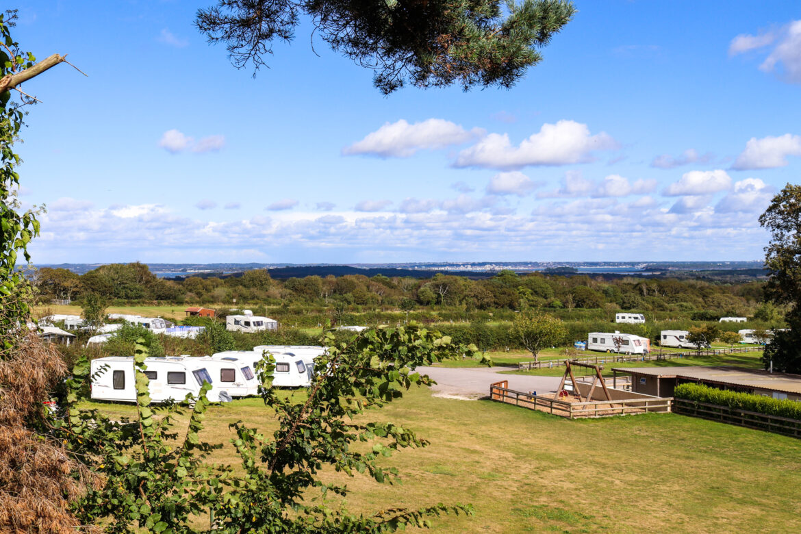 View from the trees of motorhomes and play area at East Creech Farm Campsite, with Poole Harbour and Bournemouth in the distance