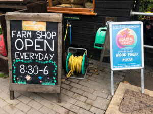 Farm shop times and Coastal Crust pizza signage at Norden Farm and Campsite