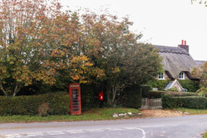 Red telephone box and letterbox next to thatched cottage on a street in East Creech village