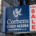 For Sale sign by Corbens Swanage attached to brick wall