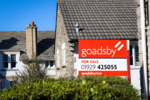 A 'For Sale' sign by Goadsby on a residential road in Swanage
