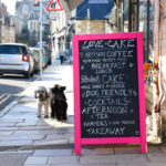two dogs outside Lovel Cake in Swanage, with brunch, takeaway and dog-friendly sign outside