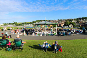 People in camping chairs listening to Swanage Town Band performance